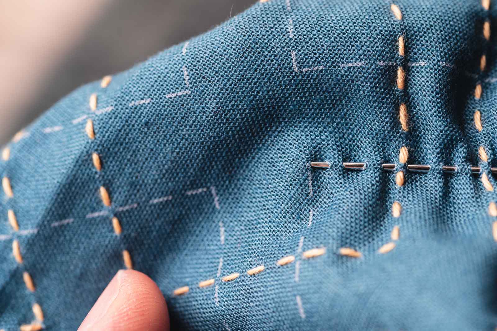 Sashiko needle piercing through teal cloth in 13 places