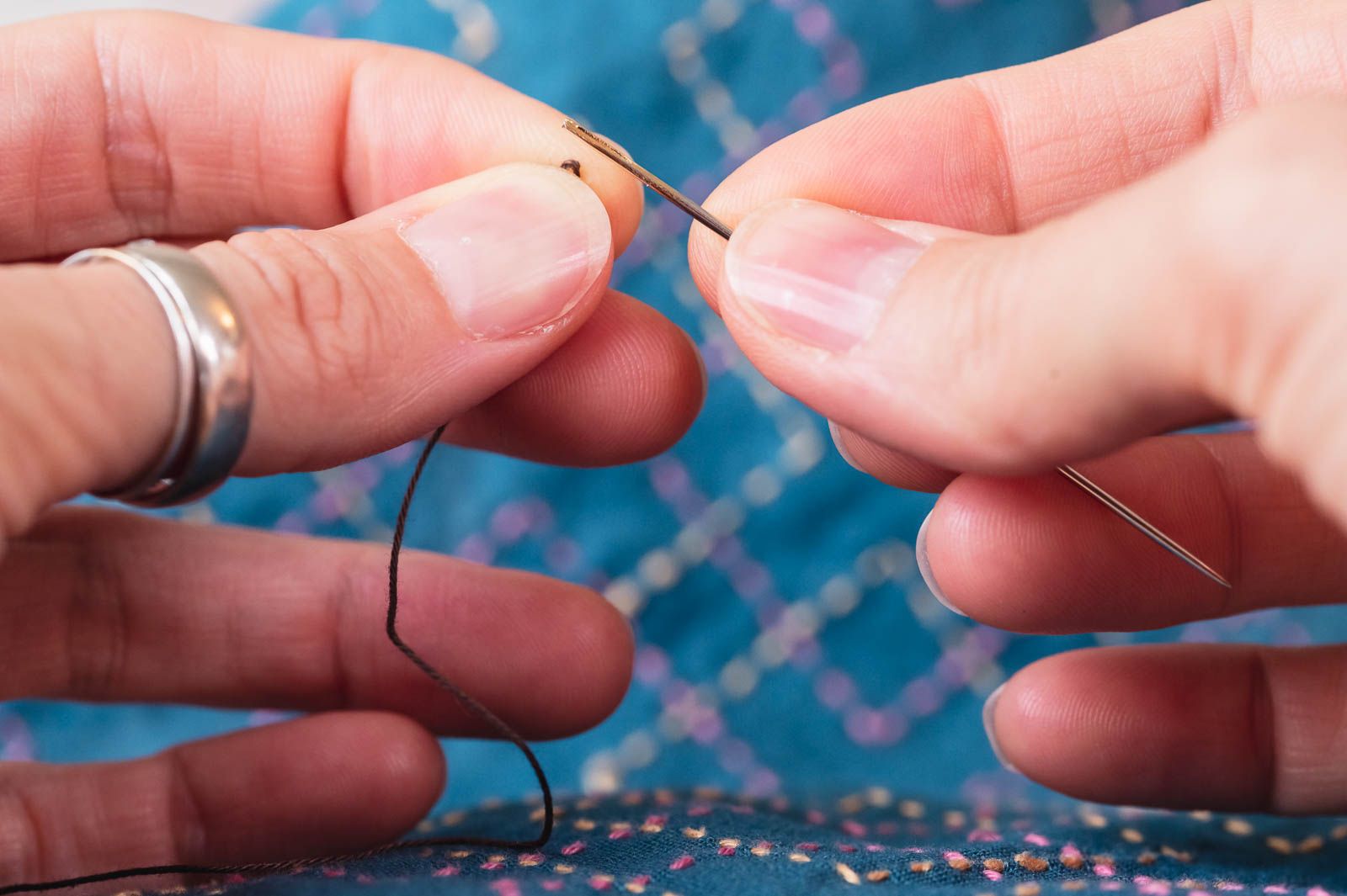 Two hands threading a thread loop through a needle's eye