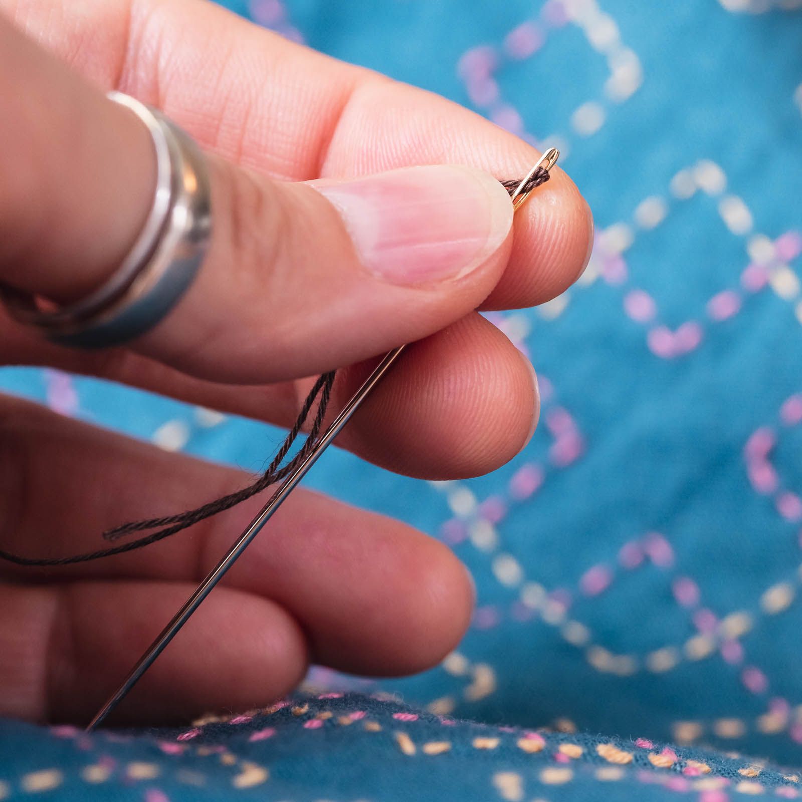 Hand holding a needle with a loop of sashiko thread peeking through the needle's eye