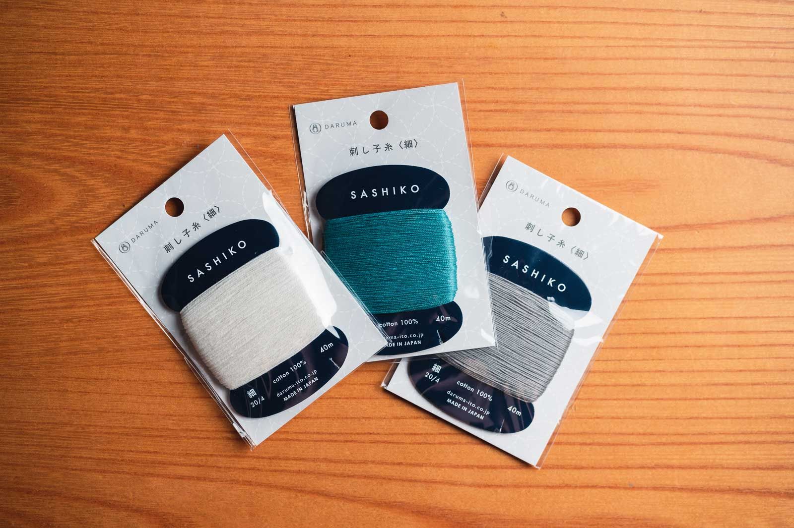 Three packages of thread by Daruma in the colors white, teal and gray