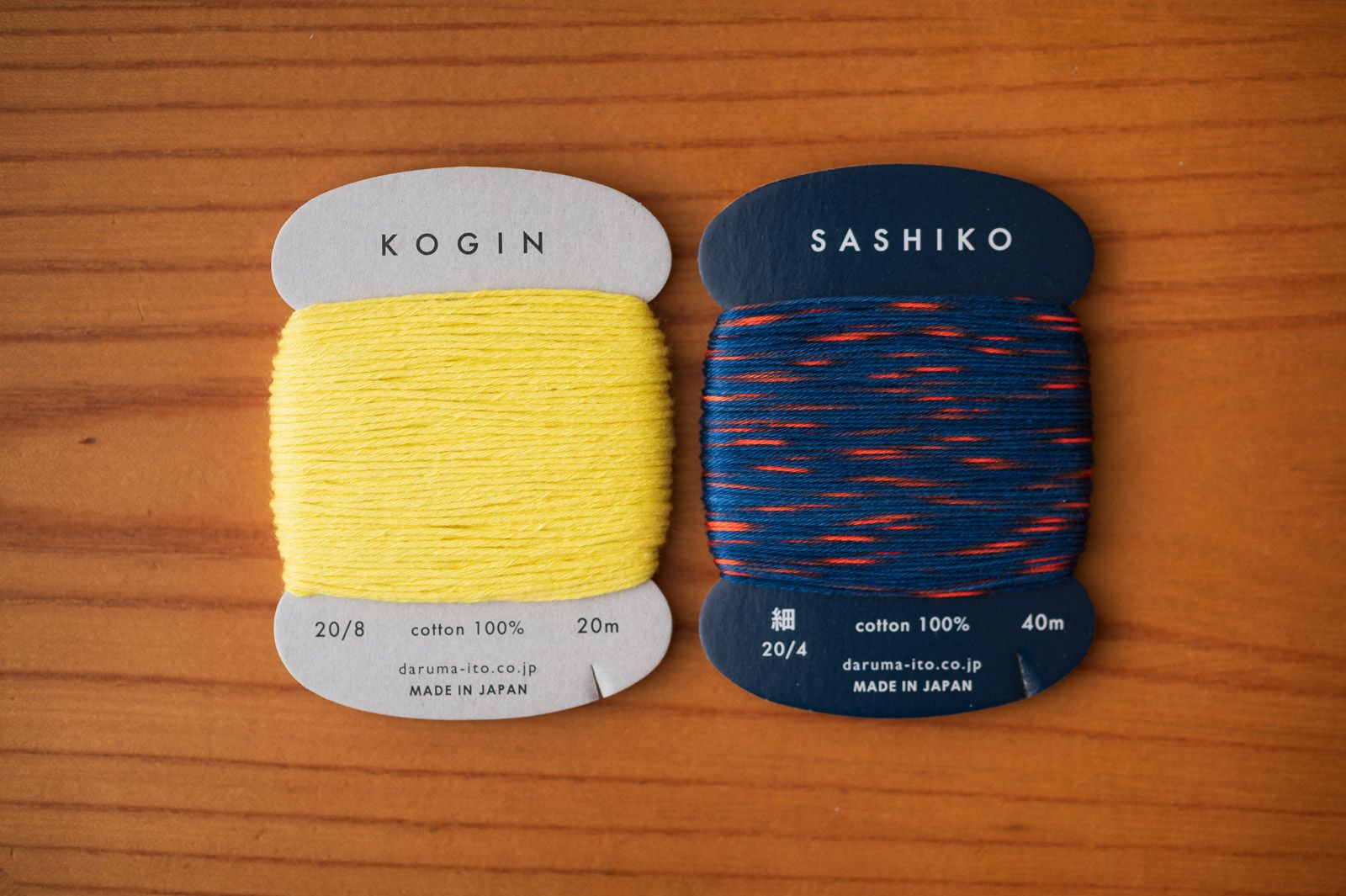 Yellow kogin thread and variegated sashiko thread in read and blue by Daruma on a table