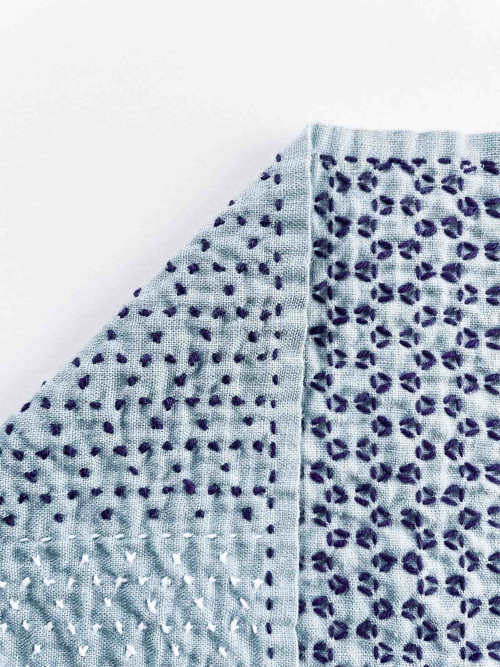 Front and back of a blue sashiko cloth with white and purple stitches.