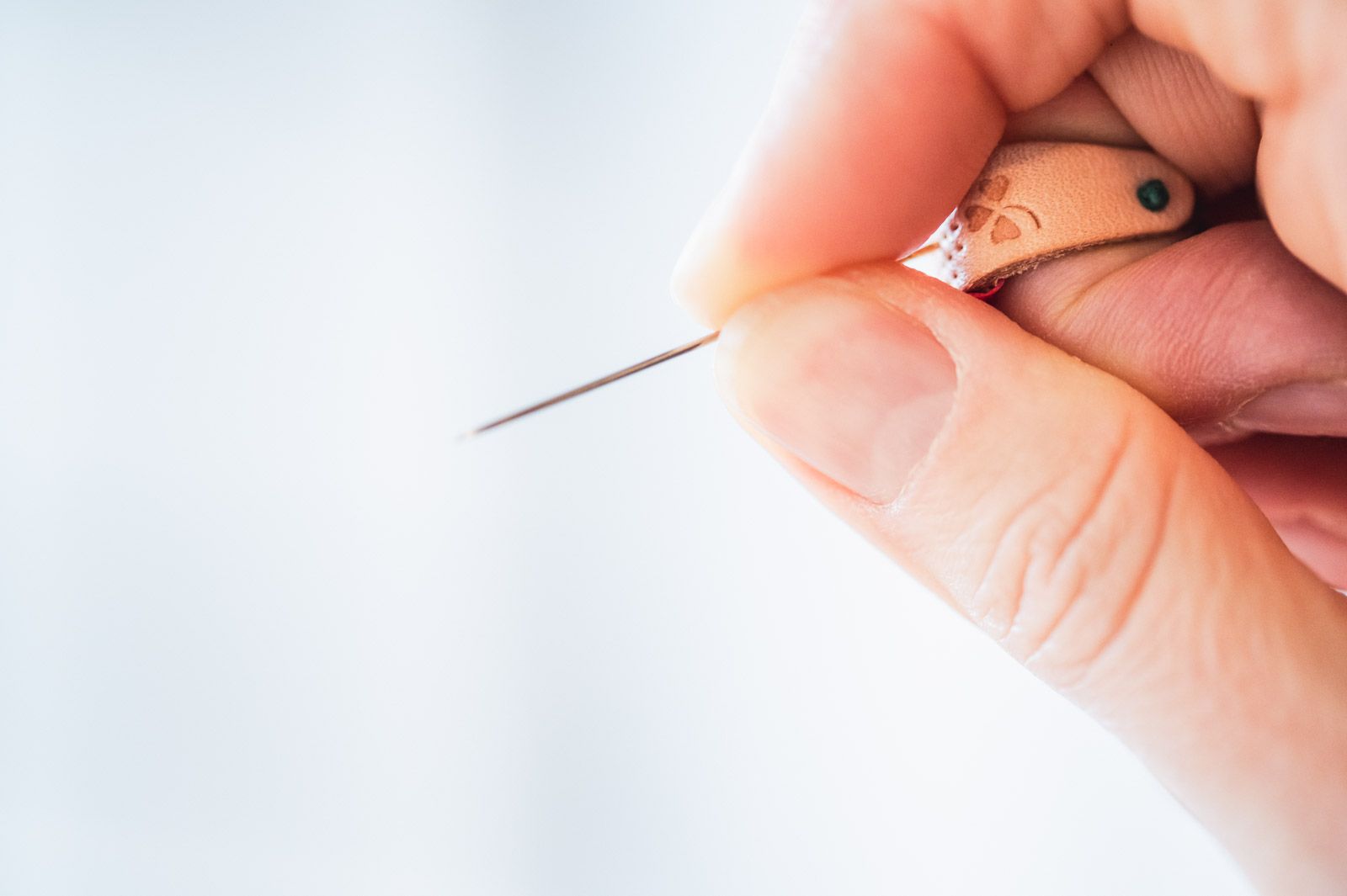 A leather ring thimble worn on the second limb of the middle finger with a needle held between thumb and index finger against it.