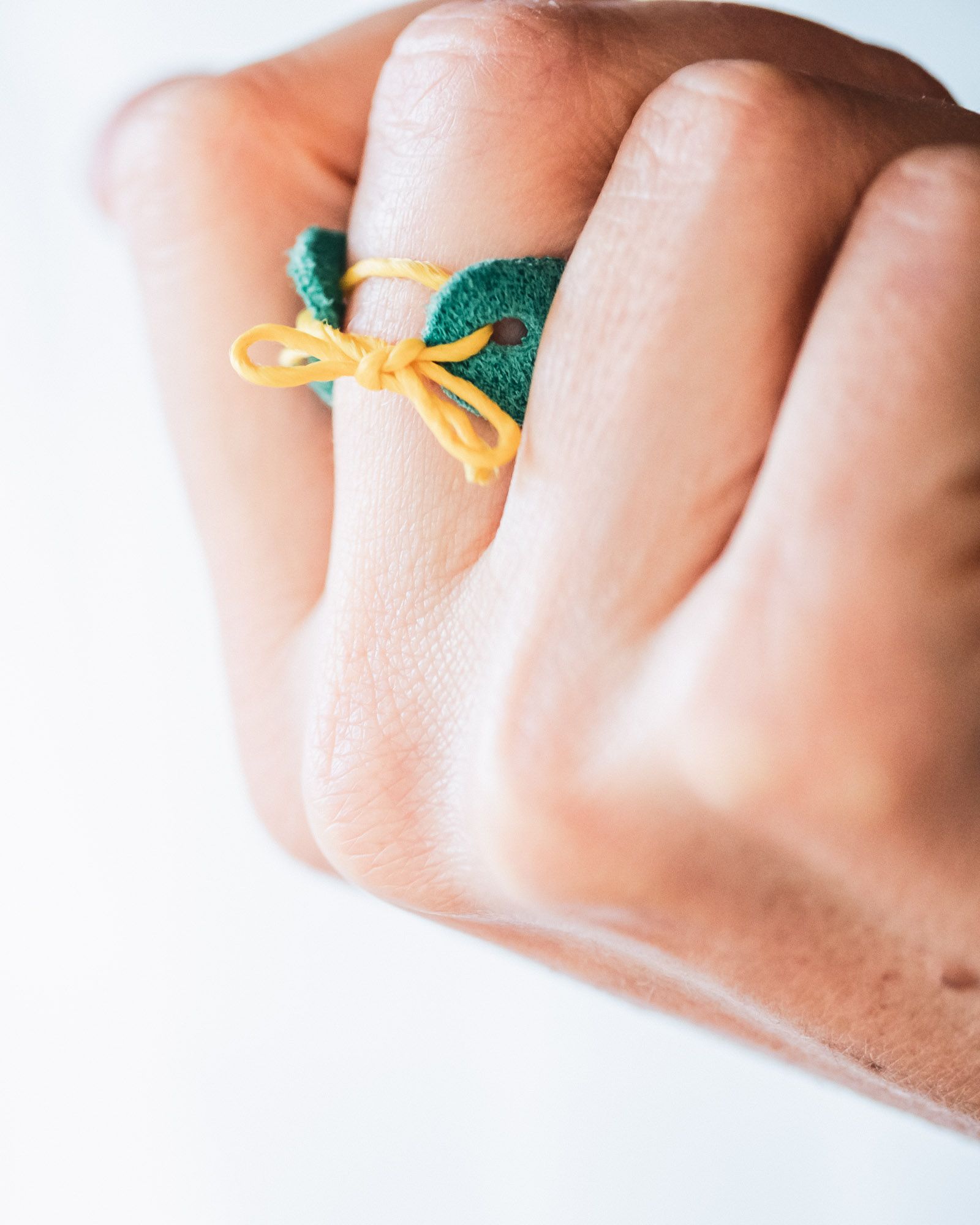 Leather palm thimble held together by a yellow string tied in a ribbon to perfectly fit the wearer's finger