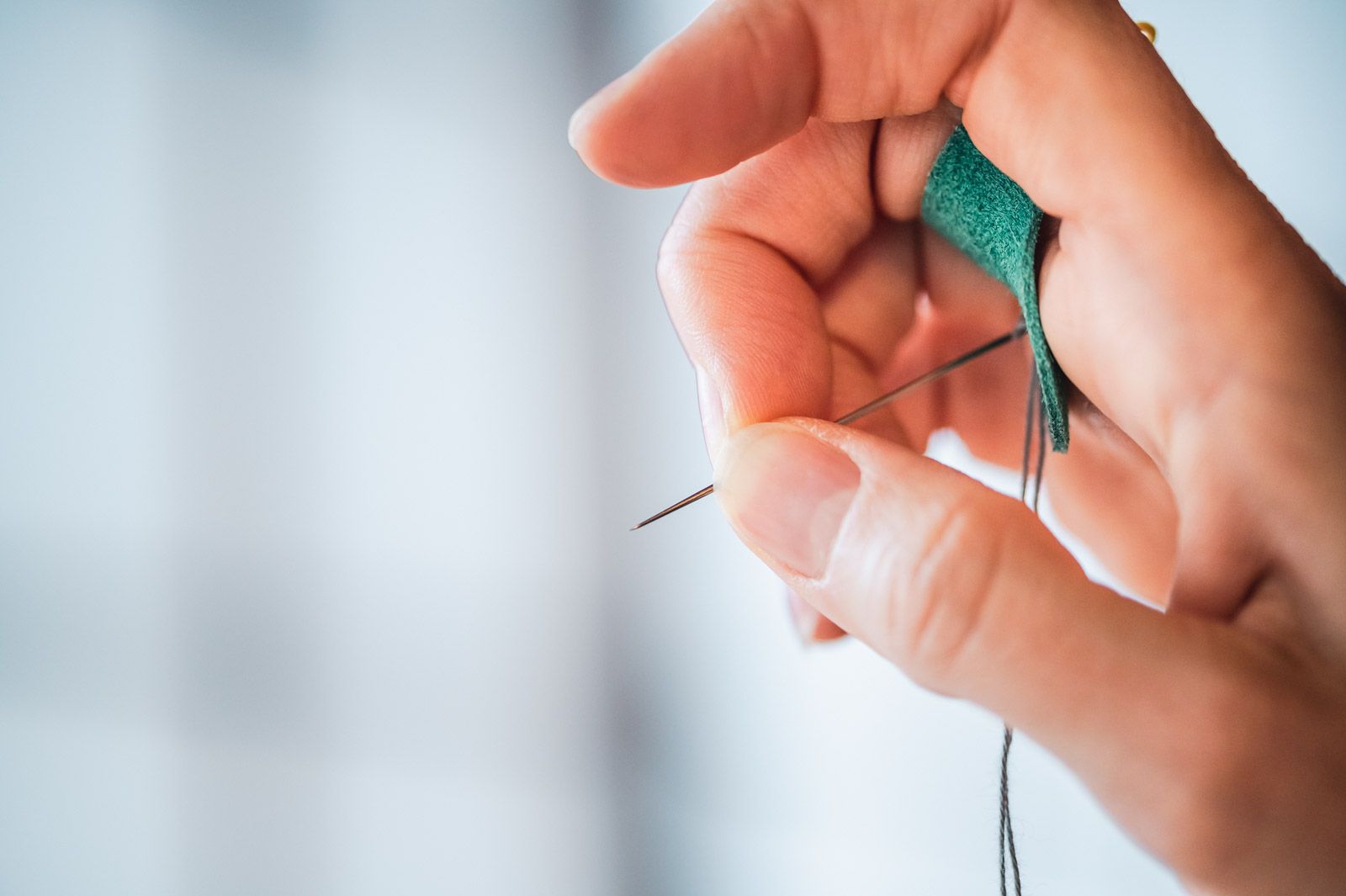 Middle finger and thumb holding a needle whose blunt end is resting against a leather palm thimble