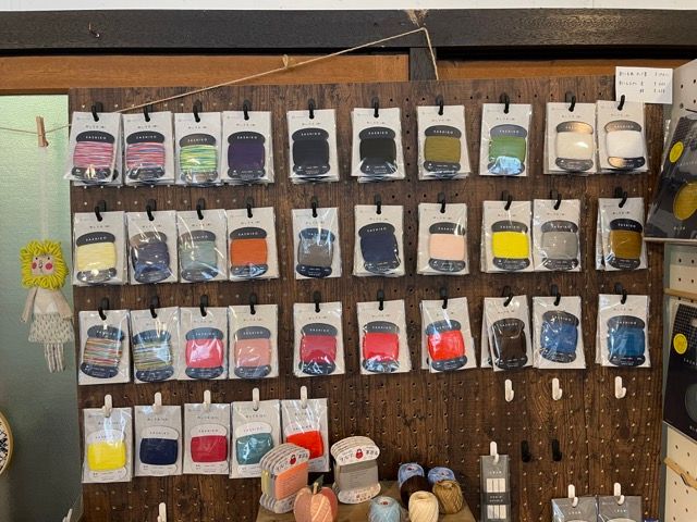 Different colored sashiko thread by daruma hanging on a wall at a store.