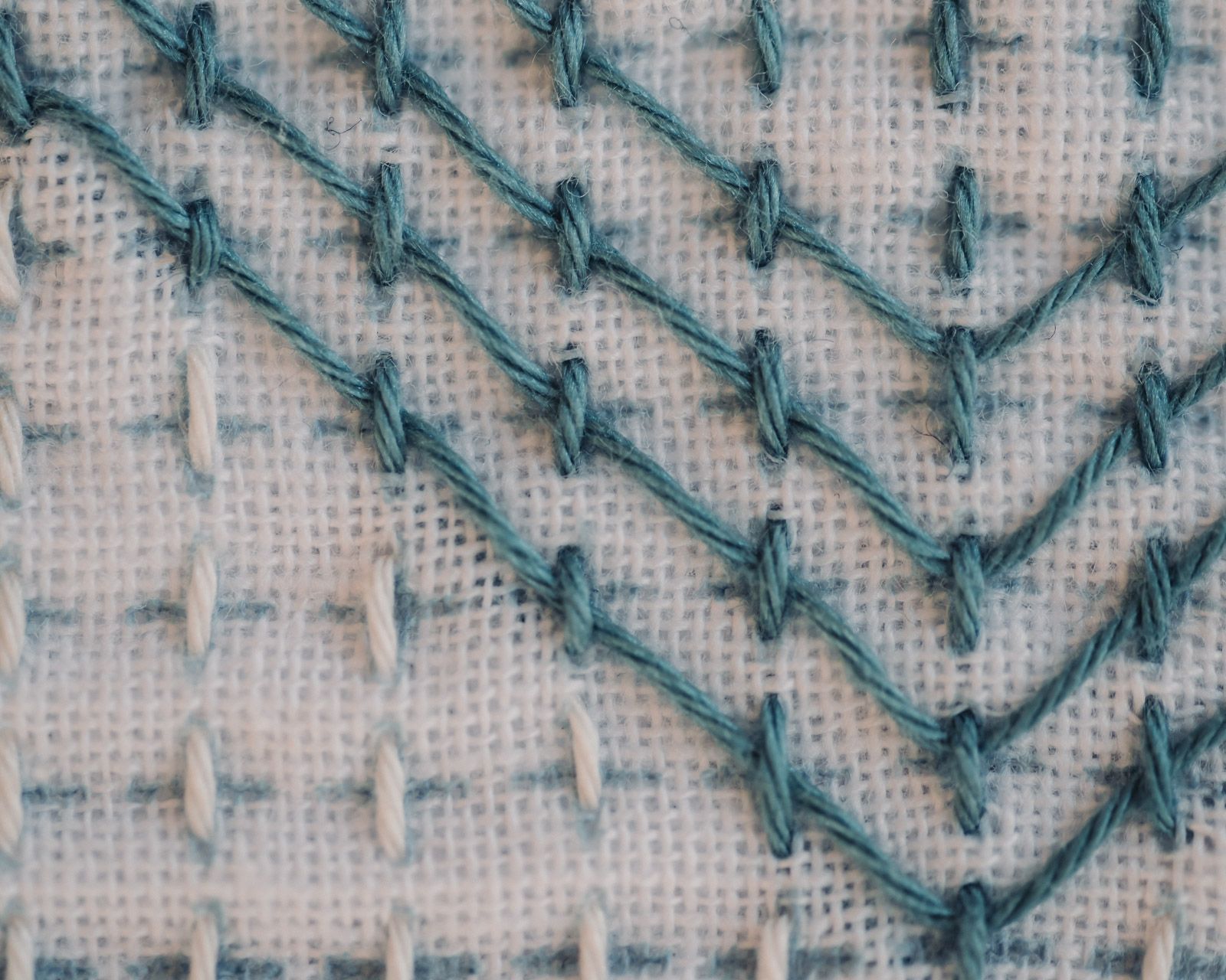 Sashiko stitches on white cloth close up with visible grid lines.