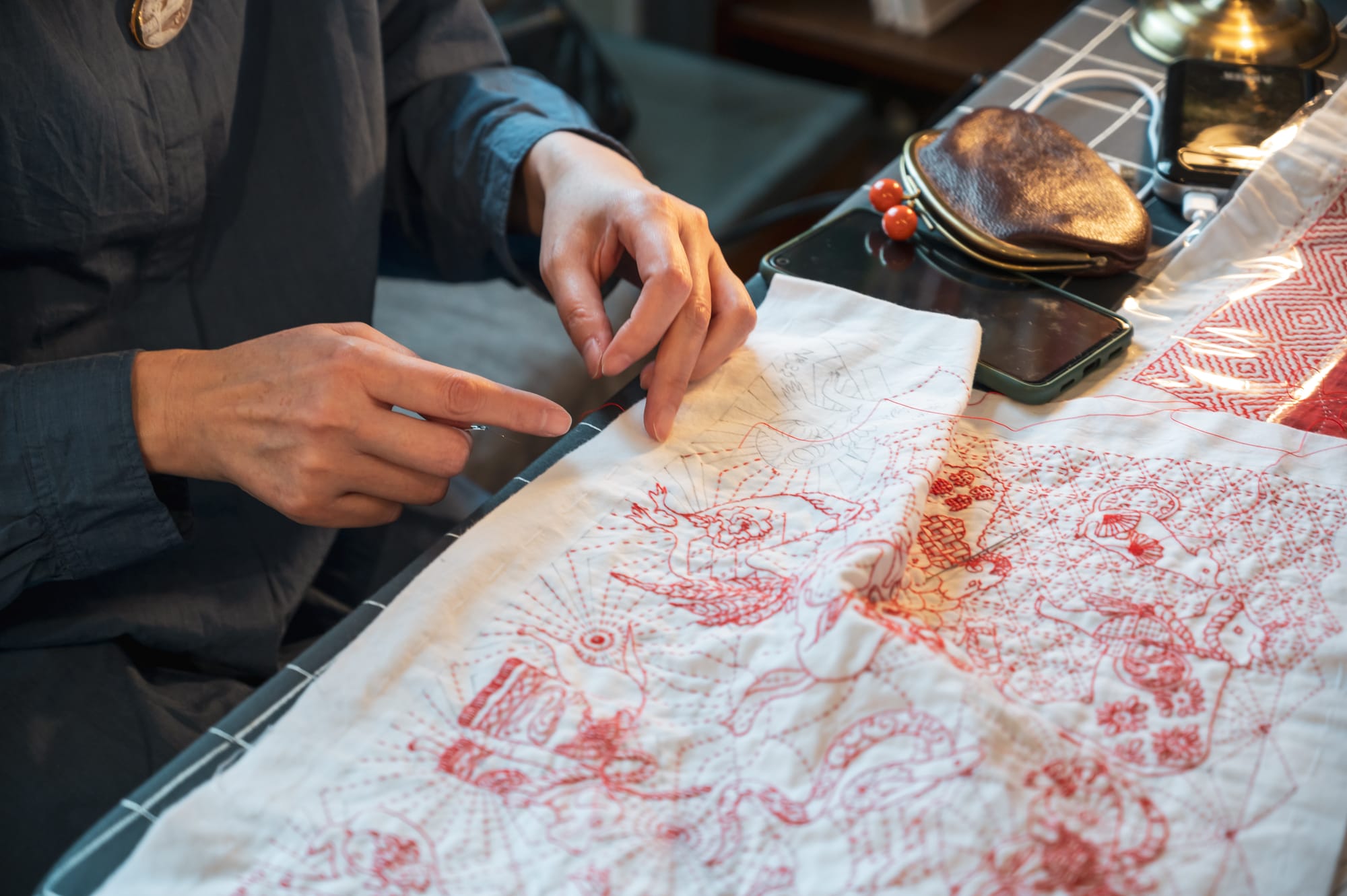 Sashiko artist Chiebaa-chan explaining her design while working on a self-designed zodiac design in red thread on white.