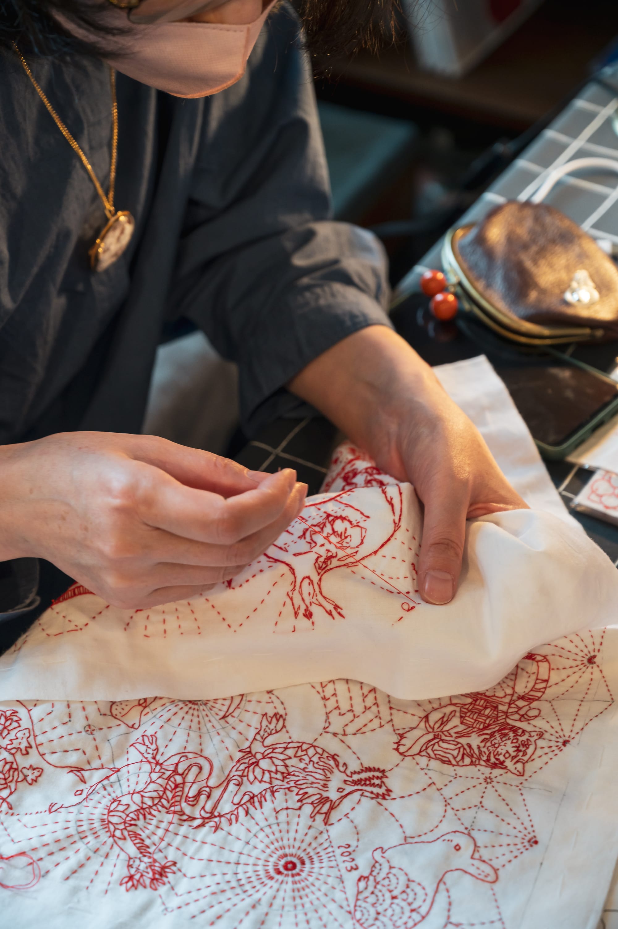 Sashiko artist Chiebaa-chan working on a self-designed zodiac design in red thread on white.