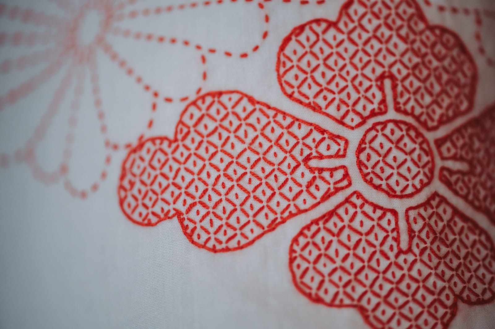 A close-up of Chiebaa's kanoko sashiko, filling in a flower in red thread on white fabric