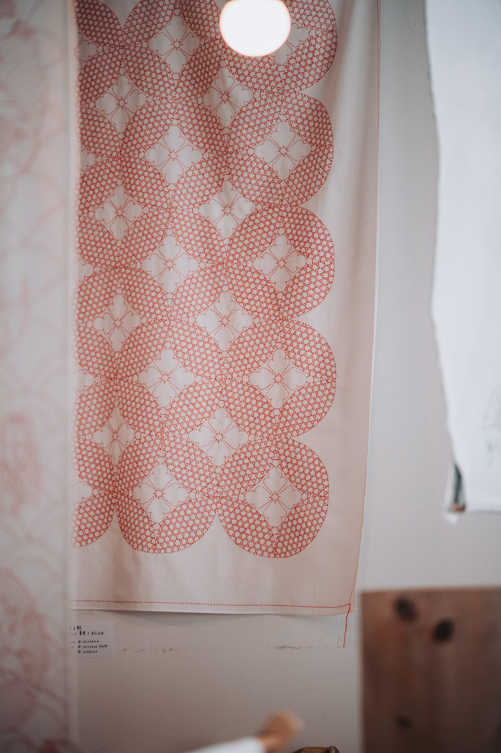 White tapestry with sashiko pattern shippo tsunagi filled in with the kagome pattern in red thread, embellished with petals