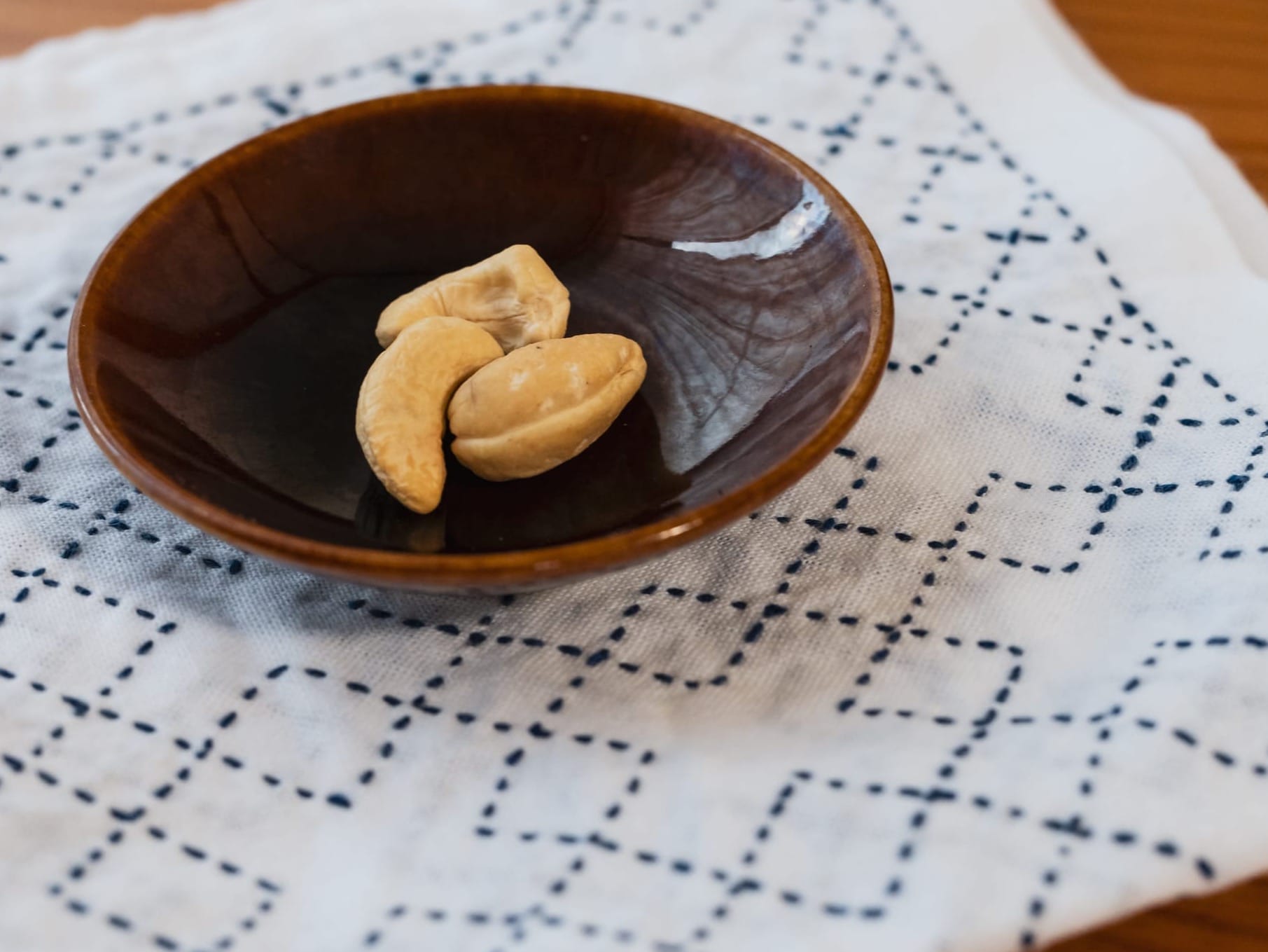 White kitchen towel with sashiko pattern kasanemasusashi in dark blue underneath a tiny dish with 3 cashew nuts on it.