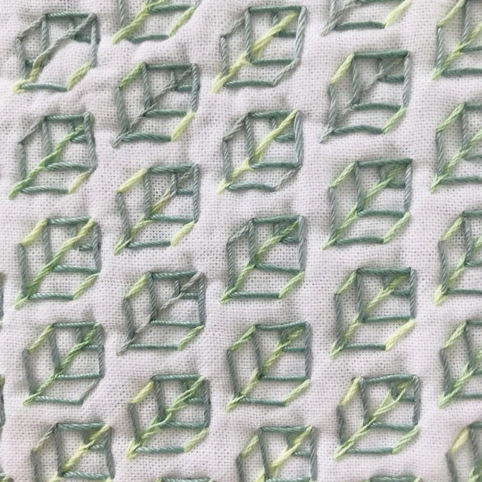 Sashiko leaf pattern stitched in shades of green on white.